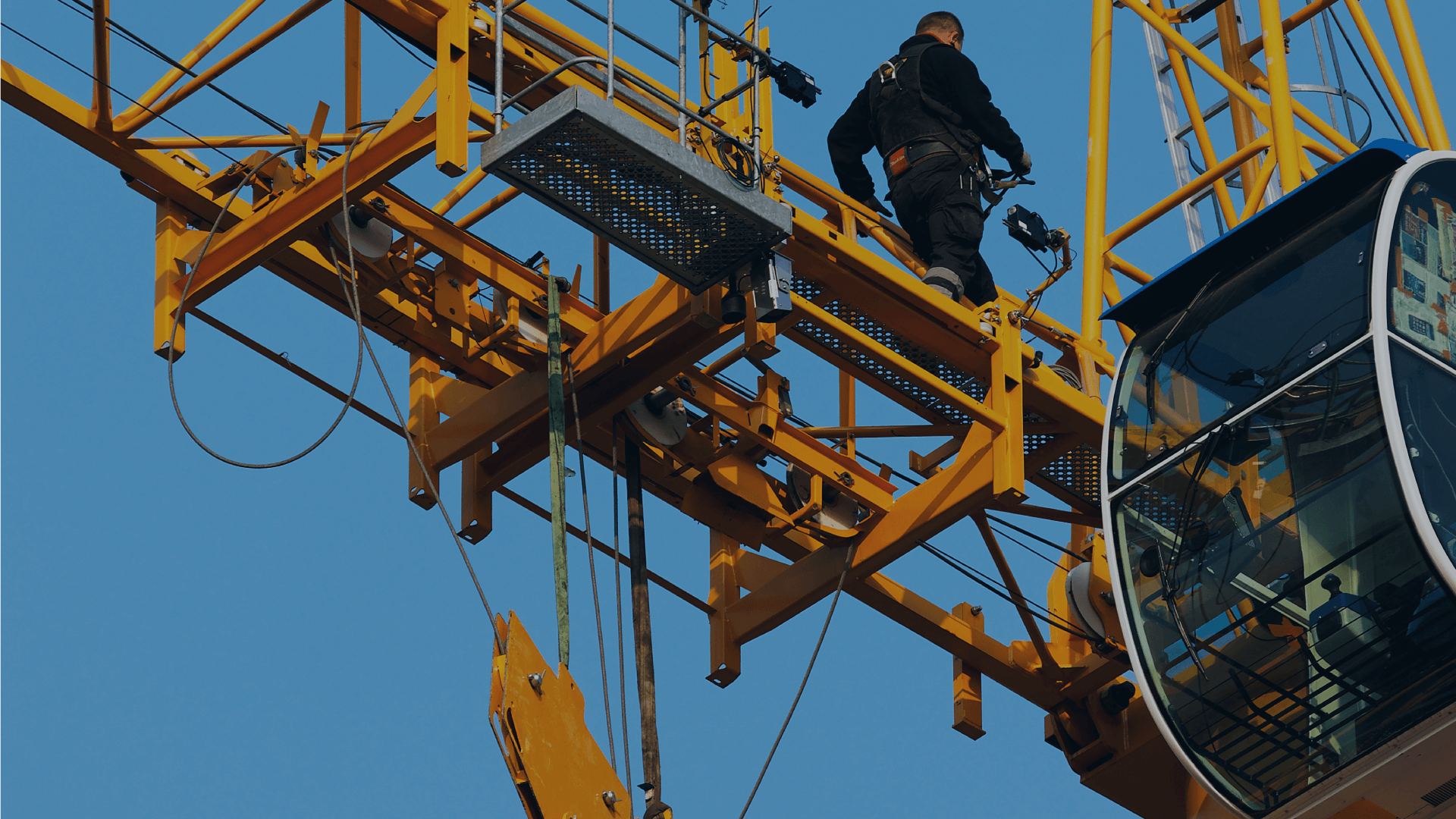 Acumatica_general-core-modules_construction-management A man atop a crane is managing a large yellow object, with a bright sky in the background.