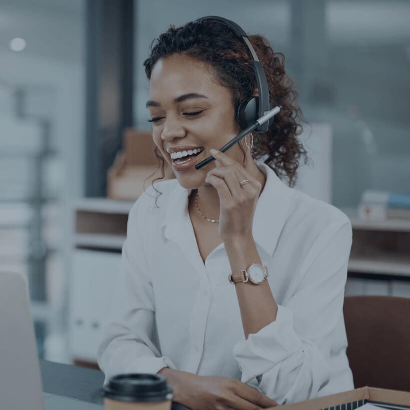 Acumatica Customer Management | A woman with a headset smiles while working on her laptop, focused and engaged in her task.